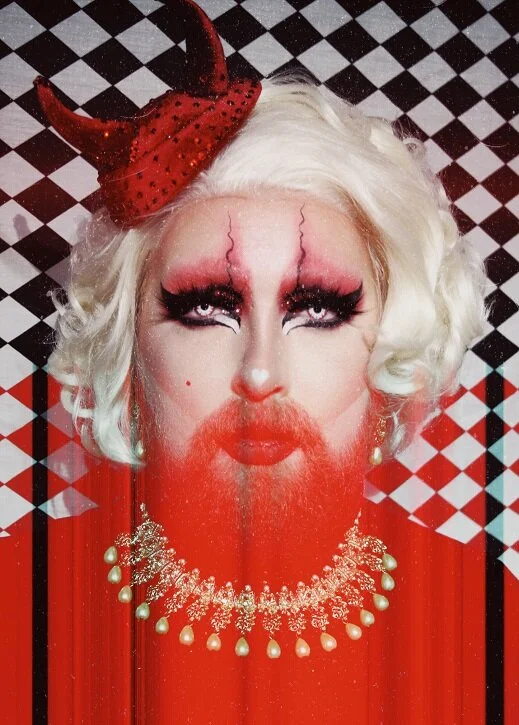 Luna Howl in red and white theatrical drag makeup with a horned headpiece
